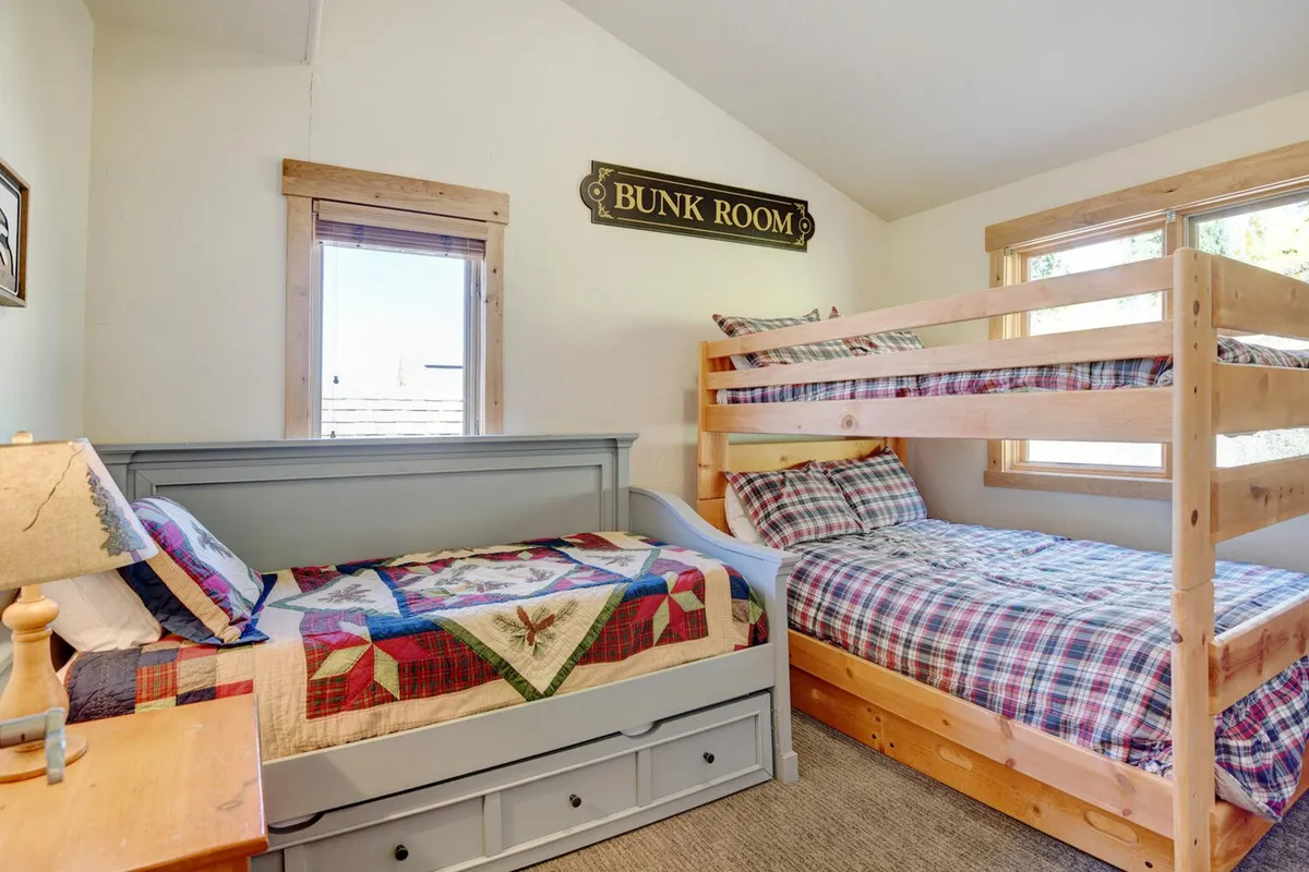 A playful, welcoming family bedroom featuring sturdy bunk beds, quilted bedspreads, wooden furniture, and windows providing natural light. The scene evokes childhood sleepovers and multigenerational stays, capturing the spirit of the dedicated family zone highlighted in the section.