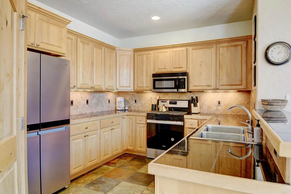 The kitchen is shown with gleaming stainless steel appliances, granite countertops, natural wood cabinetry, and slate flooring. The space exudes functionality and style, inviting guests to cook and gather around while enjoying each other's company.