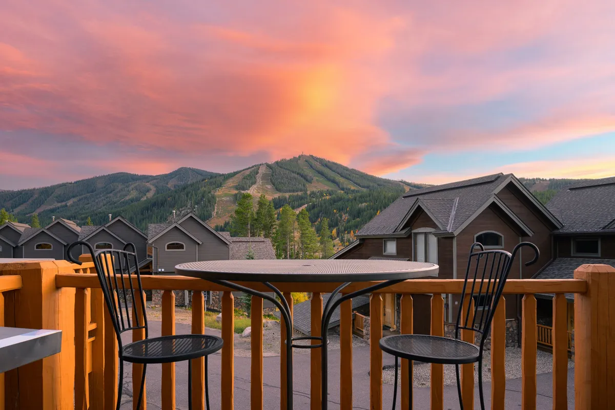 A tranquil exterior view featuring outdoor seating with a direct line of sight to a dramatic mountain range under a colorful sunset sky. The inviting setup suggests relaxation after a day of outdoor activities, highlighting the seamless blend of adventure and comfort.