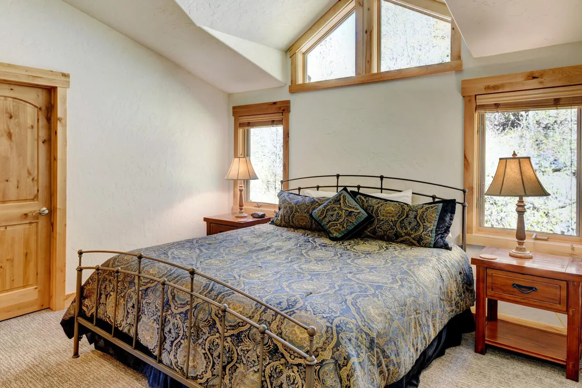 This image features another beautifully appointed bedroom with ornate bedding, large windows, and nightstands with lamps. The calm, serene mood and sunlight streaming in accentuate the restful and rejuvenating ambiance described for all bedrooms.