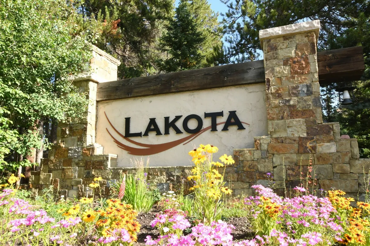 The scene showcases a beautiful stone sign surrounded by colorful flowers and lush greenery, offering a serene and picturesque entryway to the property or community.