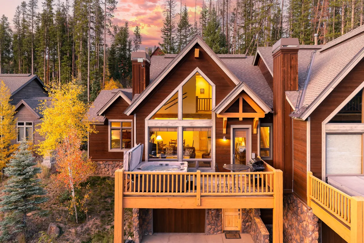The exterior of the property with large windows, a spacious deck area, warm wooden facade, and surrounding trees. The image conveys a sense of comfort and the connection between indoor and outdoor living spaces.