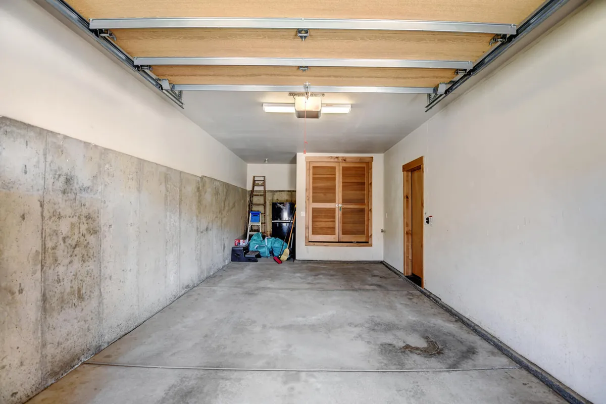 A practical storage or mudroom area with a concrete floor, wooden storage doors, a ladder, and colorful bags visible. The space is clearly designed for organizing and storing gear, tools, or personal items after a day of adventure.