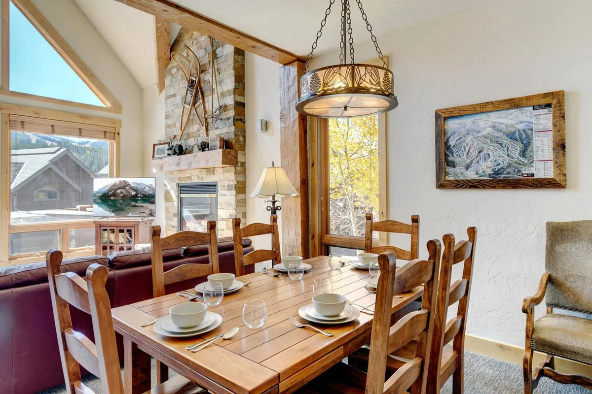 A welcoming dining area sits beside a stone fireplace, with large windows framing a striking mountain view. The table is set for family meals or game nights, and the room feels both intimate and connected to the outdoors.
