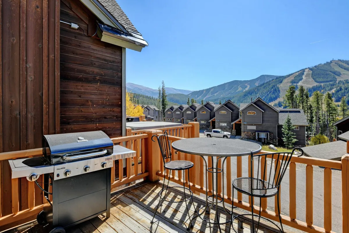 An inviting deck area equipped with a grill, outdoor dining table with chairs, and panoramic mountain views. The setting is casual and perfect for family meals or evening relaxation.